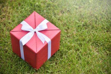 Yeşil çim zemin üzerine beyaz kurdele ile kırmızı hediye kutusu.