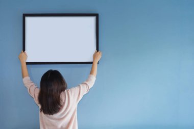 Asyalı kadın mavi duvara bir resim çerçevesi holding. 