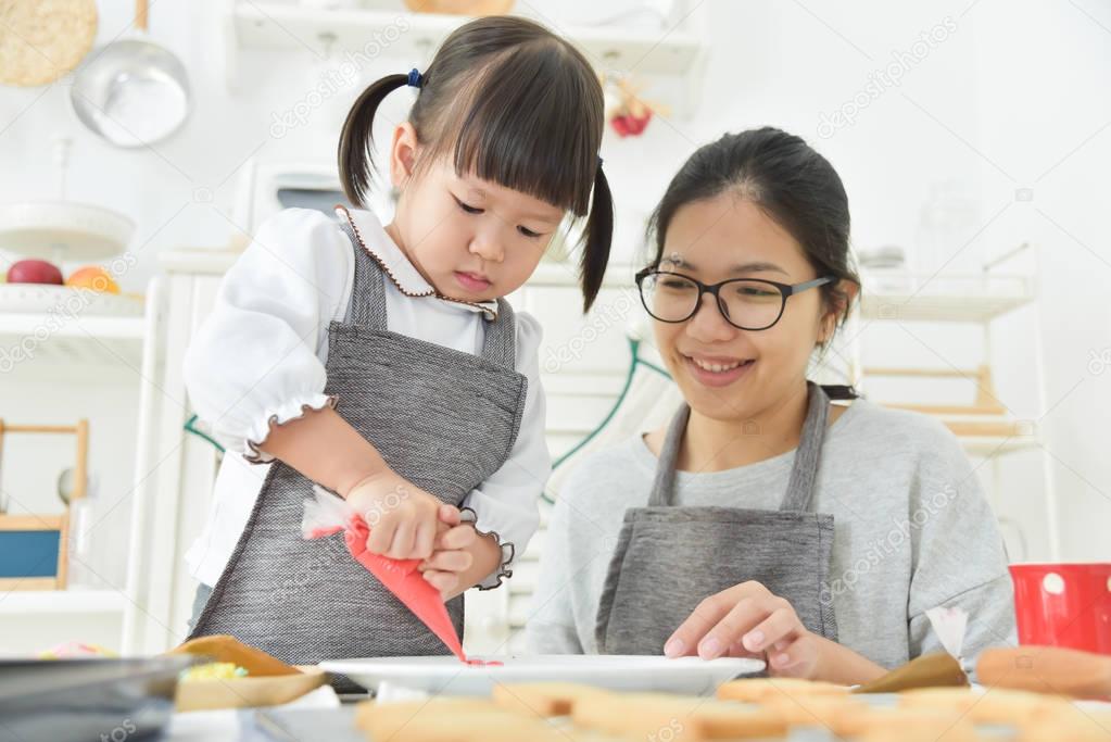 Asian Kid and young mother decorating cookies.