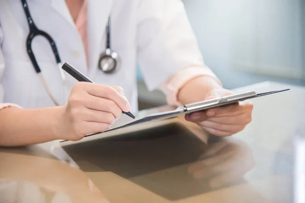 Female doctor is writing something on clipboard. — Stock Photo, Image