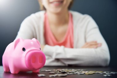 Pembe kumbara ve madeni paralar ile gülümseyen kadın masada. 