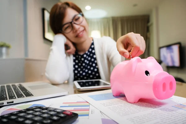 Mujer poner moneda en rosa alcancía . — Foto de Stock