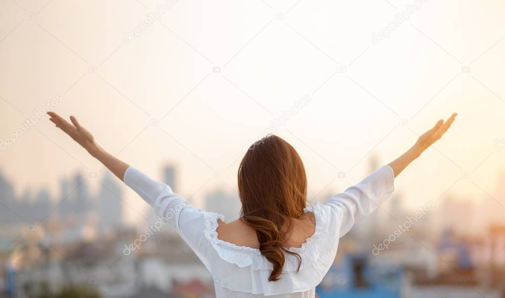 Asian woman raised hands up in the air over city background whil