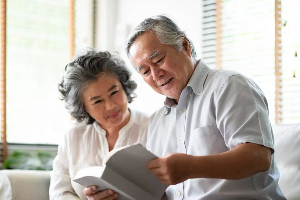 Asiatique couple sénior sont assis sur canapé et la lecture d'un livre . — Photo