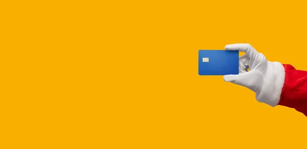 La mano de Santa Claus que sostiene la tarjeta de crédito azul en amarillo o naranja es —  Fotos de Stock