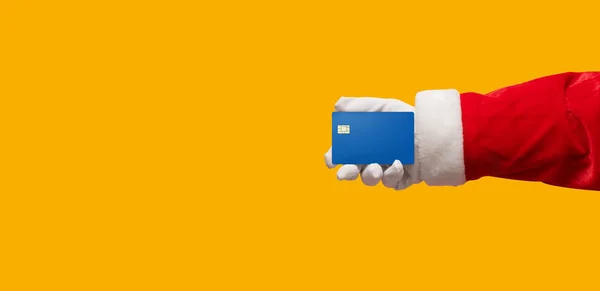 La mano de Santa Claus que sostiene la tarjeta de crédito azul en amarillo o naranja es —  Fotos de Stock