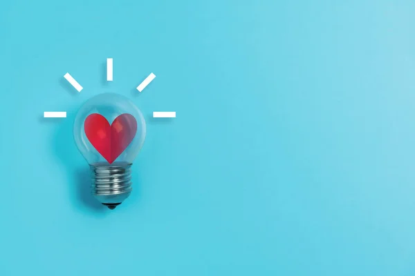 Red heart in light bulb on blue background with copy space. — Stock Photo, Image