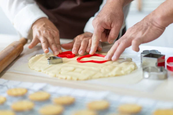 Close up Senior Couple Hands making cookies with red cutters in — Stock Photo, Image