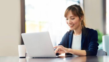 Laptop kullanan mutlu genç iş kadını kafede online alışveriş yapıyor. Gülümseyen güzel Asyalı kadın işyerinde oturuyor ve çalışıyor. Yaşam Tarzı, Teknoloji, İnternet, Kablosuz İletişim.