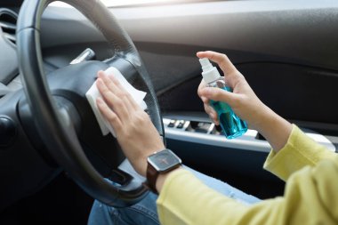 Yeşil gömlekli Asyalı kadın, direksiyonda dezenfektan alkol spreyi ve beyaz bez mendil kullanarak arabasında salgın koronavirüs ya da Coronavirüs 'ü önlüyor. Yüzeylere dokunarak temizliyorum. Antiseptik, hijyen, sağlık hizmetleri..