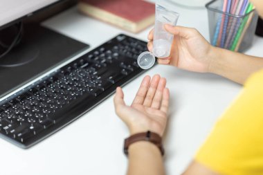 Sarı gömlekli Asyalı kadın işten sonra elini temizleyen taşınabilir el dezenfektanı kullanıyor. Coronavirus, Covid-19 'un ofiste bulunmasını önlemek için alkol temizliği ve dezenfekte uygulayan kadın..