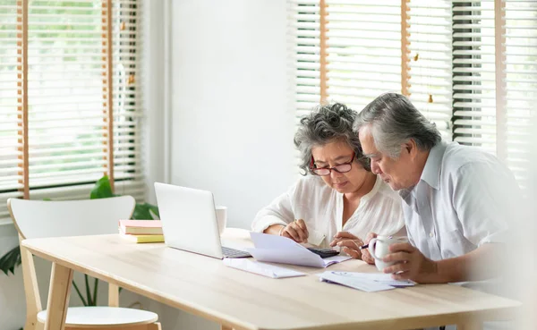 Asya 'nın üst düzey çifti hesap makinesi kullanıyor ve aile bütçesini, borçlarını hesaplıyor. Ekonomik kriz sırasında evde aylık giderleri hesaplıyor. Masadaki hesap defterine, hesap defterine, hesap defterine, makbuzuna ve dizüstü bilgisayarına bakan kıdemli adam ve kadın..