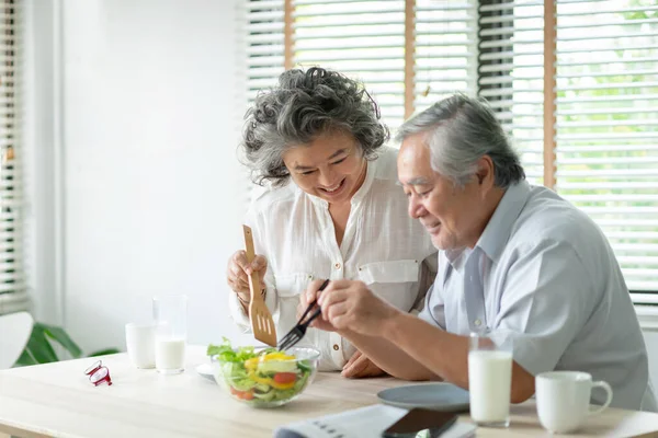Mutlu Asyalı yaşlı çift evde birlikte salata pişiriyor ve hazırlanıyor. Romantik yaşlı adam ve kadın gülerek yemeğin tadını çıkarıyor.. 