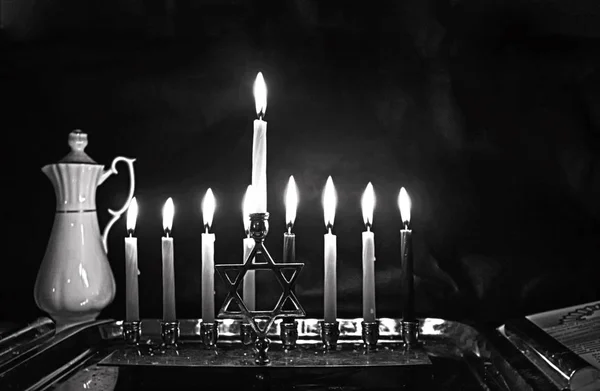 Brinnande Chanukah. Den upplysta Chanukiah. Judiska högtiden Hanukkah. Svartvitt foto. Porslin kannan med olja. — Stockfoto