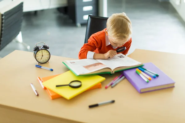 Giovane ragazzo alla scrivania in ufficio con lente di ingrandimento — Foto Stock