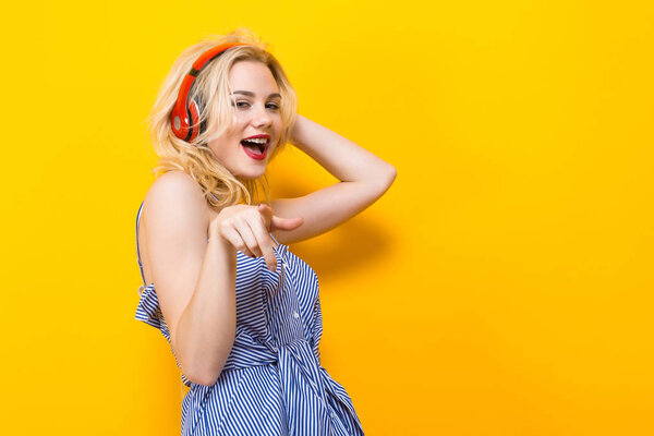 Beautiful stylish young woman listening music with headphones on yellow background