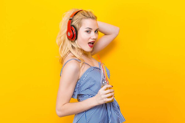 Beautiful stylish young woman with red headphones and fresh orange juice on yellow background