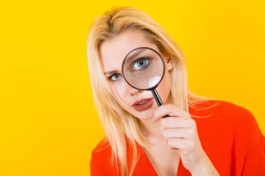 Sarı arka plan üzerinde büyüteç ile poz güzel genç kadın
