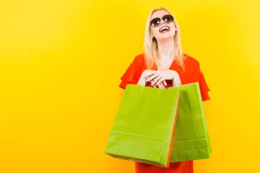 Kırmızı elbiseli sarı arka plan üzerinde renkli alışveriş torbaları ile poz güzel genç kadın
