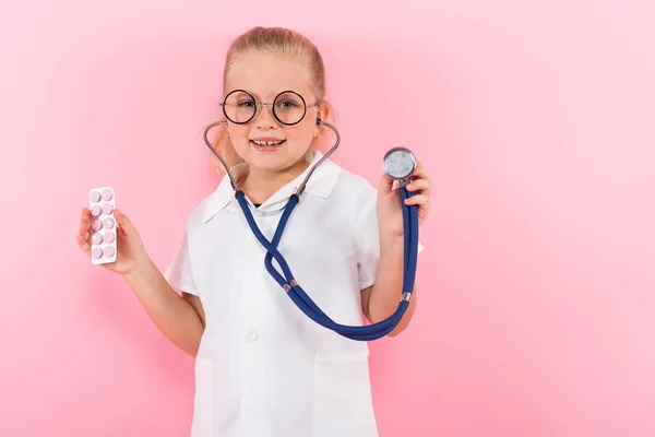 Schattig Klein Meisje Medische Uniform Met Stethoscoop Pillen Roze Achtergrond — Stockfoto