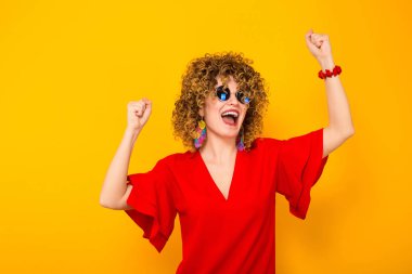 Çekici genç kıvırcık saçlı kadın kırmızı elbise ve kutlama güneş gözlüğü