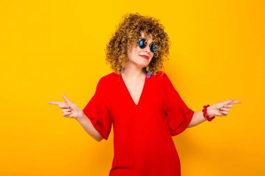 Çekici genç kıvırcık saçlı kadın kırmızı elbise ve işaret güneş gözlüğü