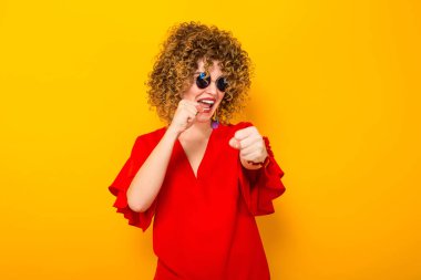 Kızgın genç kıvırcık saçlı kadın kırmızı elbise ve mücadele güneş gözlüğü