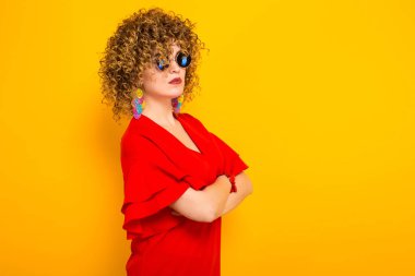 Sarı zemin üzerine kırmızı elbise ve Güneş gözlükleri çekici genç kıvırcık saçlı kadın yan görünüm