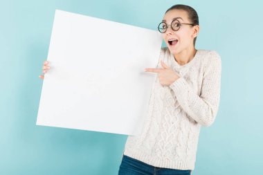 Mavi stüdyo arka planı boş afiş tutarak şık gözlük güzel kız 