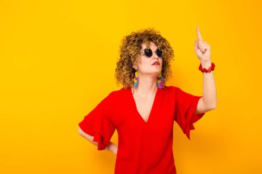 Çekici genç kıvırcık saçlı kadın kırmızı elbise ve parmağıyla işaret güneş gözlüğü