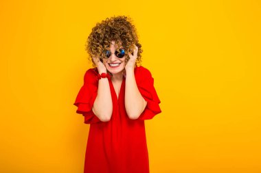 Heyecanlı çekici genç kıvırcık saçlı kadın kırmızı elbise ve güneş gözlüğü 