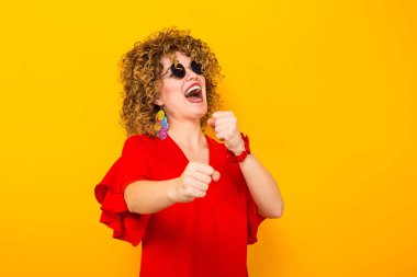 Kızgın genç kıvırcık saçlı kadın kırmızı elbise ve mücadele güneş gözlüğü