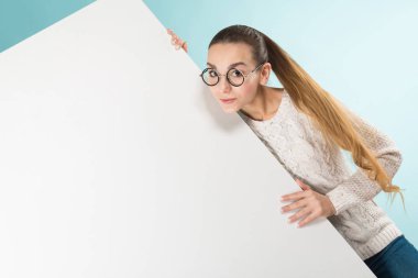 Mavi stüdyo arka planı boş afiş tutarak şık gözlük güzel kız 