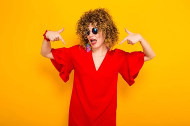 Çekici genç kıvırcık saçlı kadın kırmızı elbise ve işaret güneş gözlüğü