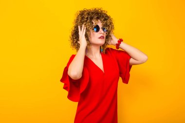 Çekici genç kıvırcık saçlı kadın kırmızı elbise ve kafasına elele güneş gözlüğü