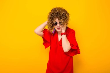 Çekici genç kıvırcık saçlı kadın kırmızı elbise ve Sarı zemin üzerine poz güneş gözlüğü 
