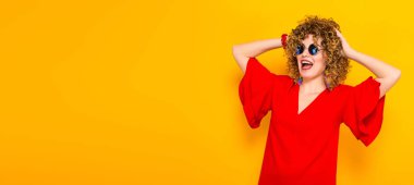 Çekici genç kıvırcık saçlı kadın kırmızı elbise ve ellerini başını tutan güneş gözlüğü