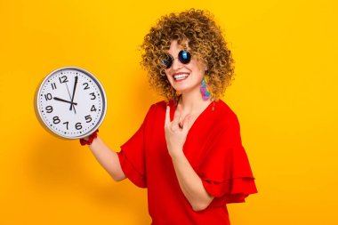 Duvar saati tutan Kırmızı elbiseli çekici genç kıvırcık saçlı kadın