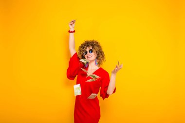 Çekici genç kıvırcık saçlı kadın kırmızı elbise ve para atma güneş gözlüğü 