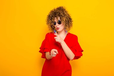 Çekici genç kıvırcık saçlı kadın kırmızı elbise ve işaret güneş gözlüğü