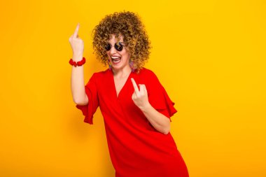 Çekici genç kıvırcık saçlı kadın kırmızı elbise ve orta parmak gösterilen güneş gözlüğü