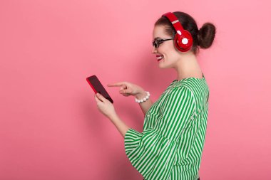 Smartphone kullanarak pembe studio arka plan üzerinde kırmızı Kulaklığımda mutlu çekici genç esmer kadın 