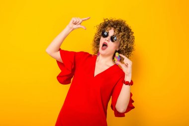 Çekici genç kıvırcık saçlı kadın kırmızı elbise ve boyutu gösteren güneş gözlüğü