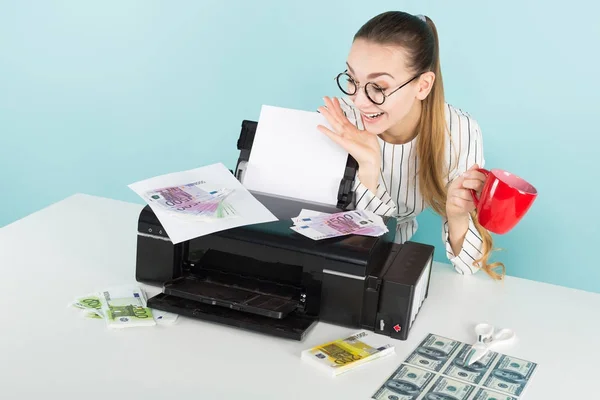 Pretty girl in stylish eyeglasses printing fake money on modern printer and holding red cup