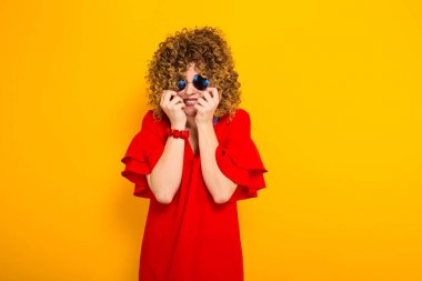 Çekici genç kıvırcık saçlı kadın kırmızı elbise ve el ele tutuşarak güneş gözlüğü duymak onun yüzünü