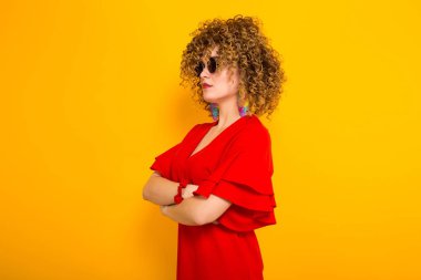 Sarı zemin üzerine kırmızı elbise ve Güneş gözlükleri çekici genç kıvırcık saçlı kadın yan görünüm