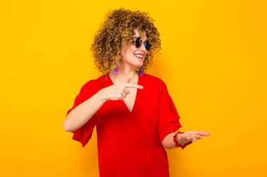 Çekici genç kıvırcık saçlı kadın kırmızı elbise ve işaret güneş gözlüğü