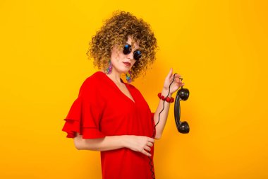 Çekici genç kıvırcık saçlı kadın kırmızı elbise ve vintage telefon tanıtıcısı tutan güneş gözlüğü