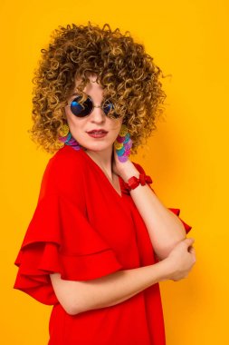Çekici genç kıvırcık saçlı kadın kırmızı elbise ve sarı arka planı poz güneş gözlüğü 