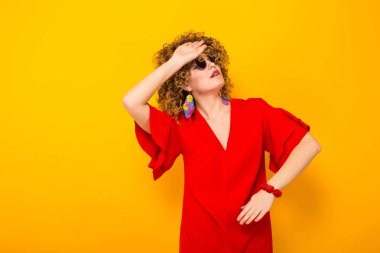 Çekici genç kıvırcık saçlı kadın kırmızı elbise ve alnında elini tutarak güneş gözlüğü